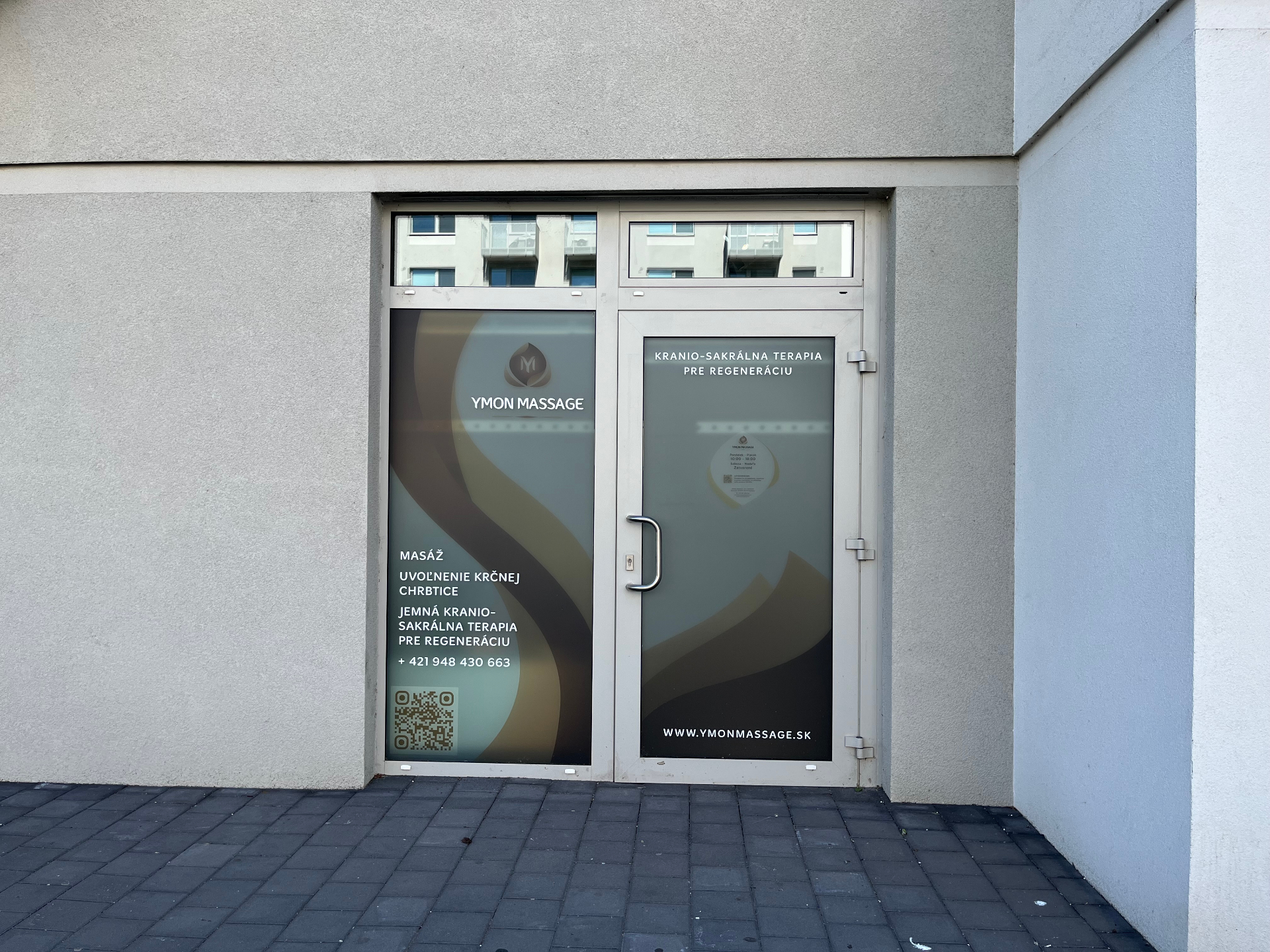Vchod do štúdia YMON masáže — presklené dvere s logom YMON MASSAGE a nápisom Kranio-sakrálna terapia pre regeneráciu na Ivanskej ceste 32/A.